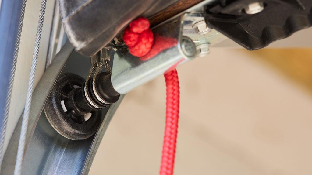 Black nylon roller attached to a zinc-plated hinge with a red rope connected.