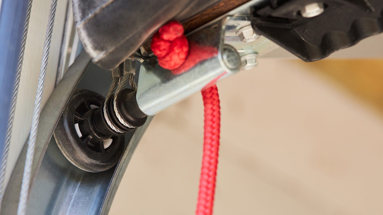 Black nylon roller attached to a zinc-plated hinge with a red rope connected.