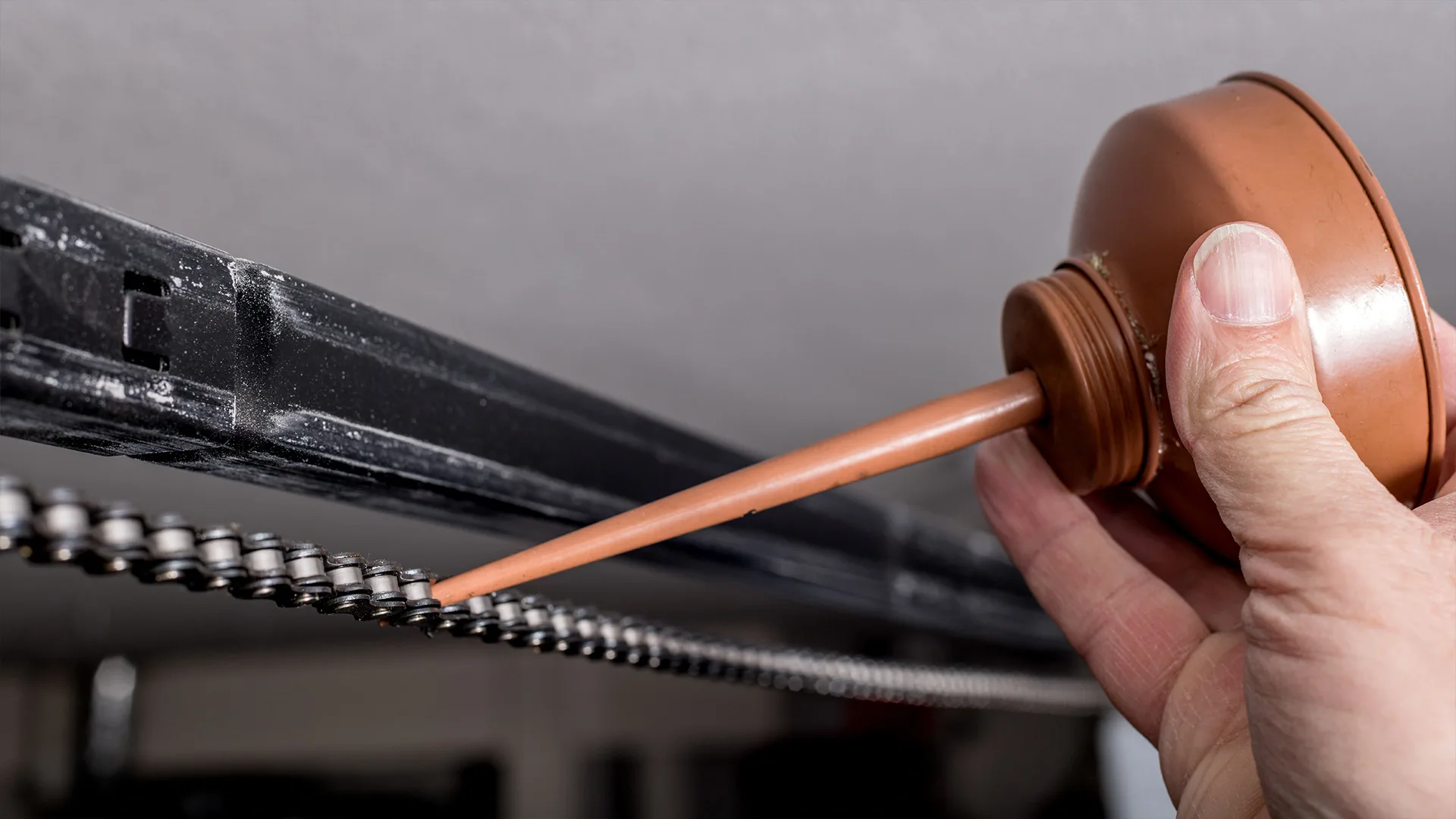  person squeezing oil onto a garage door opener chain to help garage door move smoother